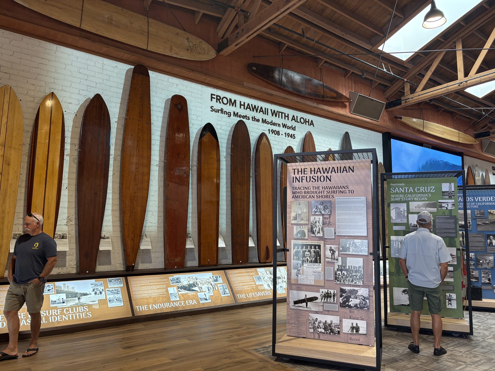 A surfboard shaping bay inside the Surfing Heritage and Culture Center on Ocean Avenue, lined with vintage surf film posters and board racks. The center hosts the festival's opening night party.
