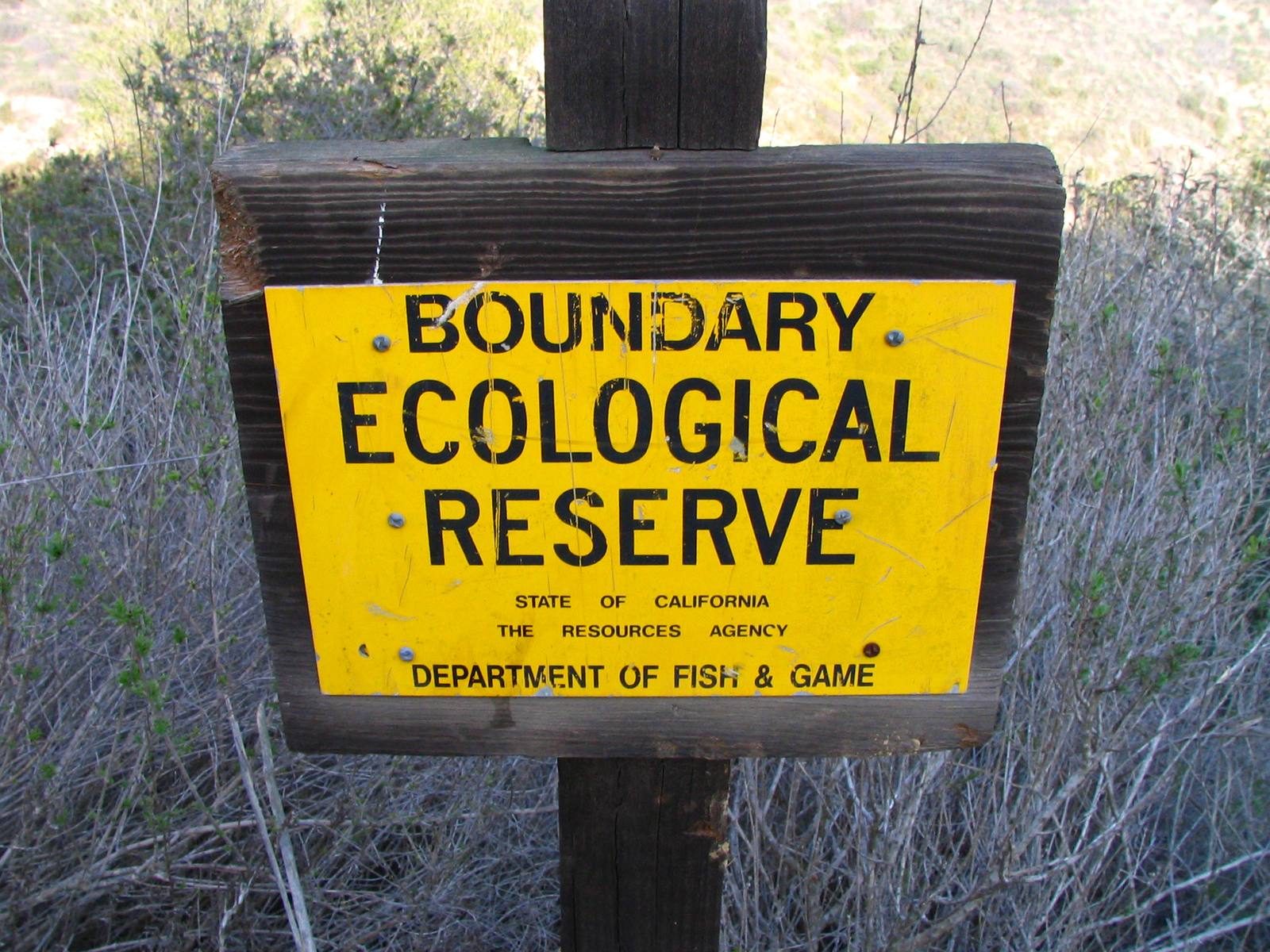 A California Ecological Reserve boundary sign stands in the scrub of Laguna Canyon, marking the protected lands under discussion.