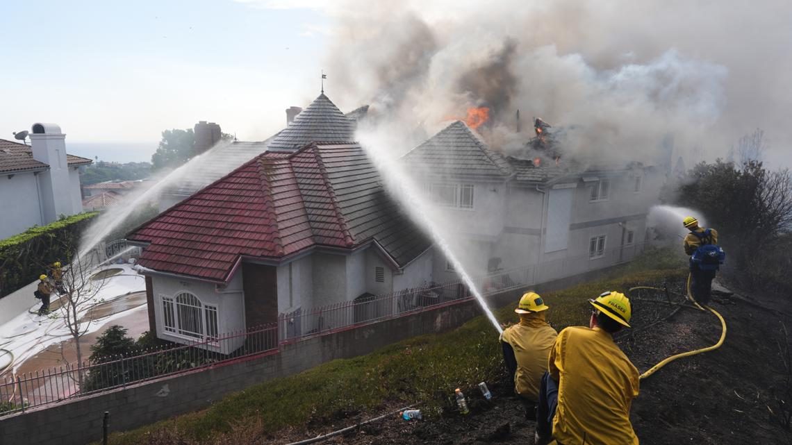 Firefighters spray water on a burning home from the hillside above it in San Juan Capistrano. Crews attacked the fire from the ground and the air on Friday.