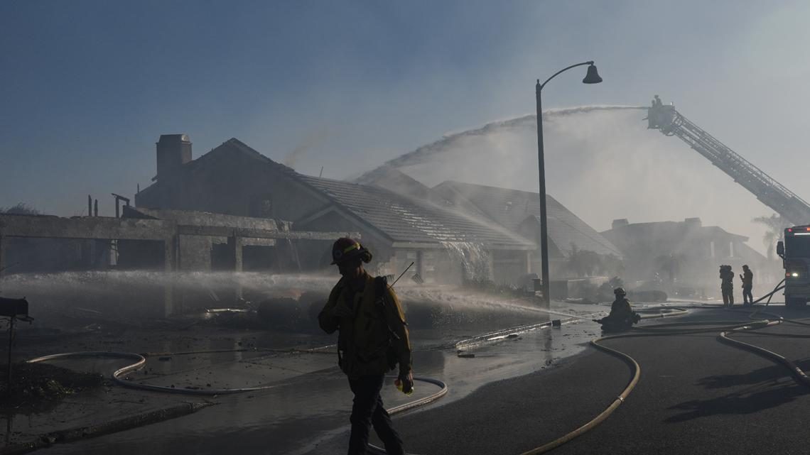 A firefighter walks past a burned out home as a ladder truck sprays water on damaged houses. About 16,000 people were ordered to evacuate in San Clemente and San Juan Capistrano.